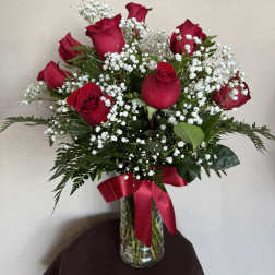 Red roses with white baby's breath in a glass vase tied with a red ribbon