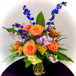 Orange roses and blue flowers in a glass vase