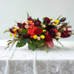 Low floral centerpiece with red roses, calla lilies, and yellow accents in a wooden container