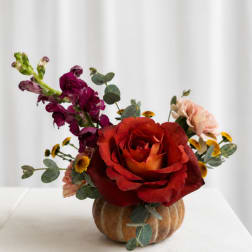Red rose arrangement with purple and peach flowers in a small pumpkin vase