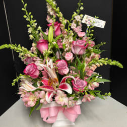 Pink and white floral arrangement in a white vase with a pink ribbon