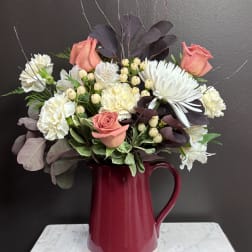 Pink roses and white flowers arranged in a burgundy pitcher vase
