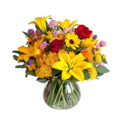 Mixed bouquet of yellow lilies, red roses, and daisies in a glass vase