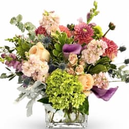Mixed bouquet in a clear square vase with pink, peach, purple, and green blooms