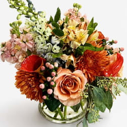 Mixed bouquet in a clear glass vase with peach, orange, pink, and cream blooms