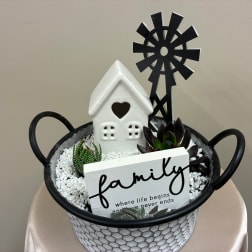 Succulent arrangement in a handled basket with a small house and family sign