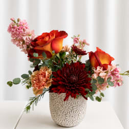 Mixed bouquet with orange-red roses and burgundy chrysanthemums in a patterned vase