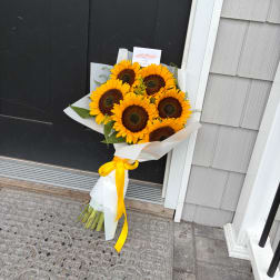 Bouquet of sunflowers wrapped in white paper with a yellow ribbon