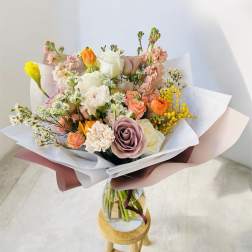 Mixed pastel bouquet in a glass vase on a small stool