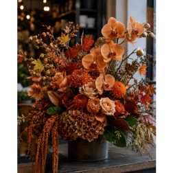Autumn floral arrangement with orange orchids and roses in a dark vase