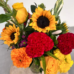 Bright mixed bouquet with sunflowers, roses, and carnations in a glass vase