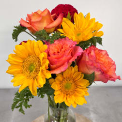 Bouquet of orange roses and yellow sunflowers in a clear glass vase