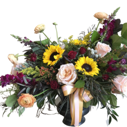 Mixed bouquet with sunflowers, roses, and purple blooms in a dark vase