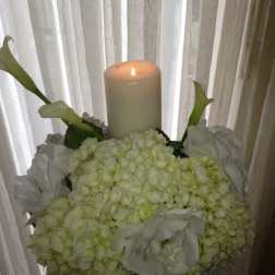 White floral arrangement with a lit pillar candle and calla lilies