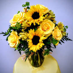 Yellow roses and sunflowers arranged in a glass vase
