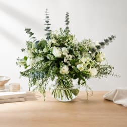 White floral arrangement in a clear glass vase with tall eucalyptus stems
