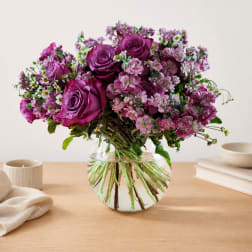 Purple roses and pink flowers arranged in a clear glass vase