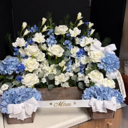 White and blue floral arrangement in a wooden box with ribbon bows