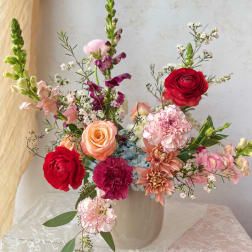 Mixed bouquet of roses, carnations, and snapdragons in a white vase