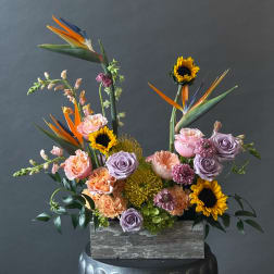 Tropical floral arrangement with sunflowers, roses, and bird of paradise in a wooden box