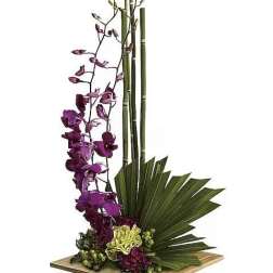 Tall orchid arrangement with purple blooms and green bamboo in a wooden base