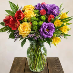 Mixed bouquet of roses, lilies, and purple blooms in a glass vase