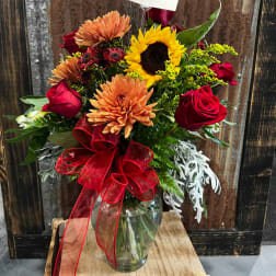 Bouquet of sunflowers, roses, and mums in a glass vase with a red ribbon