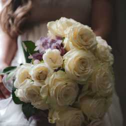 Bride holding a bouquet of cream roses and pale purple flowers