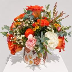 Orange roses and mixed blooms in a leaf-patterned vase