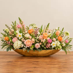Low floral centerpiece in a gold bowl with pink, peach, white, and orange blooms