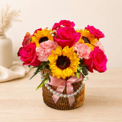 Pink roses and sunflowers in a wicker basket with a pink ribbon
