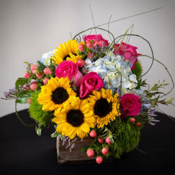Bright bouquet with sunflowers, pink roses, and blue hydrangeas in a wooden box