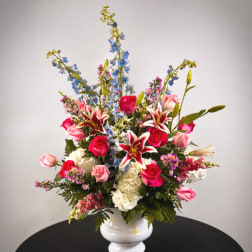 Tall mixed bouquet in a white vase with roses, lilies, and blue delphinium