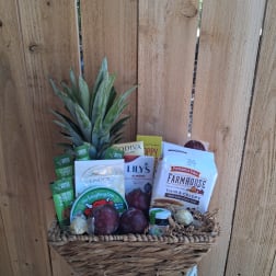 Gift basket with snacks, chocolates, and a pineapple top against a wooden fence