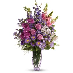 Mixed purple and pink flowers arranged in a tall glass vase