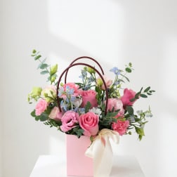 Pink and blue mixed flower arrangement in a pink gift box with ribbon handles
