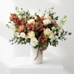 Bouquet of cream roses, orchids, and white blooms in a ribbed white vase