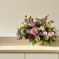 Mixed bouquet in a woven basket with pink, yellow, and purple flowers
