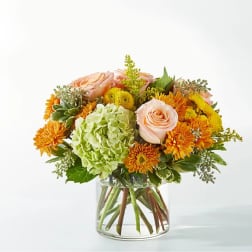 Mixed bouquet of peach roses, green hydrangea, and orange mums in a glass vase