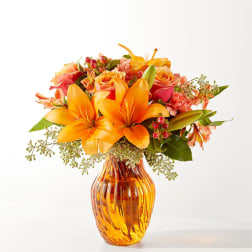 Orange lilies and mixed roses in an amber glass vase