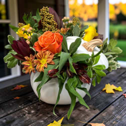 Autumn floral arrangement in a white pumpkin vase with orange and yellow blooms