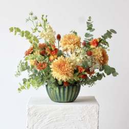 Orange and yellow mixed flower arrangement in a green ceramic vase
