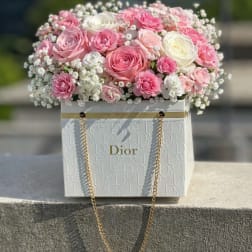 Pink and white roses arranged in a Dior gift box with gold chain handles.
