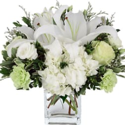 White lilies and roses in a clear glass vase with green accents