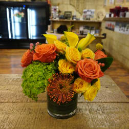 Orange and yellow roses in a glass vase with green hydrangea