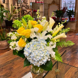 Yellow roses, white lilies, and blue hydrangea in a glass vase