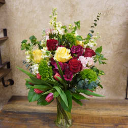 Mixed bouquet of roses, tulips, and white blooms in a glass vase