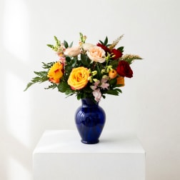 Mixed roses in a blue glass vase on a white pedestal