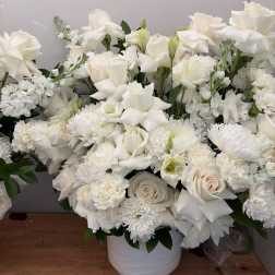 White floral arrangement in a white vase with roses, lilies, and mums