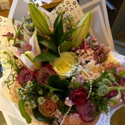 Mixed bouquet with roses, lilies, and small filler flowers in decorative wrap